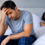 Hombre preocupado en el dormitorio, representación de la disfunción eréctil y su impacto en la pareja